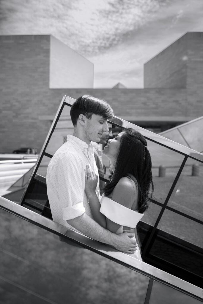 Black and white photo shows a woman looking up at a man, as they both stand in front of artistic glass pyramids at the National Gallery of Art