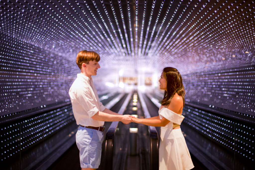 Two people hold hands facing each other, with hundreds of LED lights twinkling behind them from the National Gallery of Art walkway